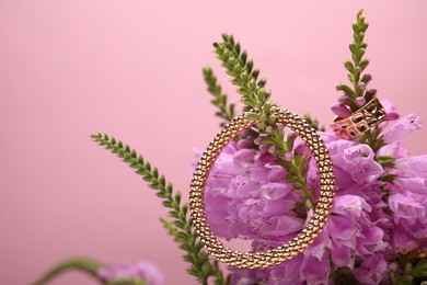 Photo of Stylish gold ring, bracelet and beautiful flowers against pink background, closeup. Space for text