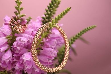 Photo of Stylish gold ring, bracelet and beautiful flowers against pink background, closeup. Space for text