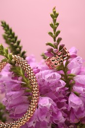 Photo of Stylish gold ring, bracelet and beautiful flowers against pink background, closeup