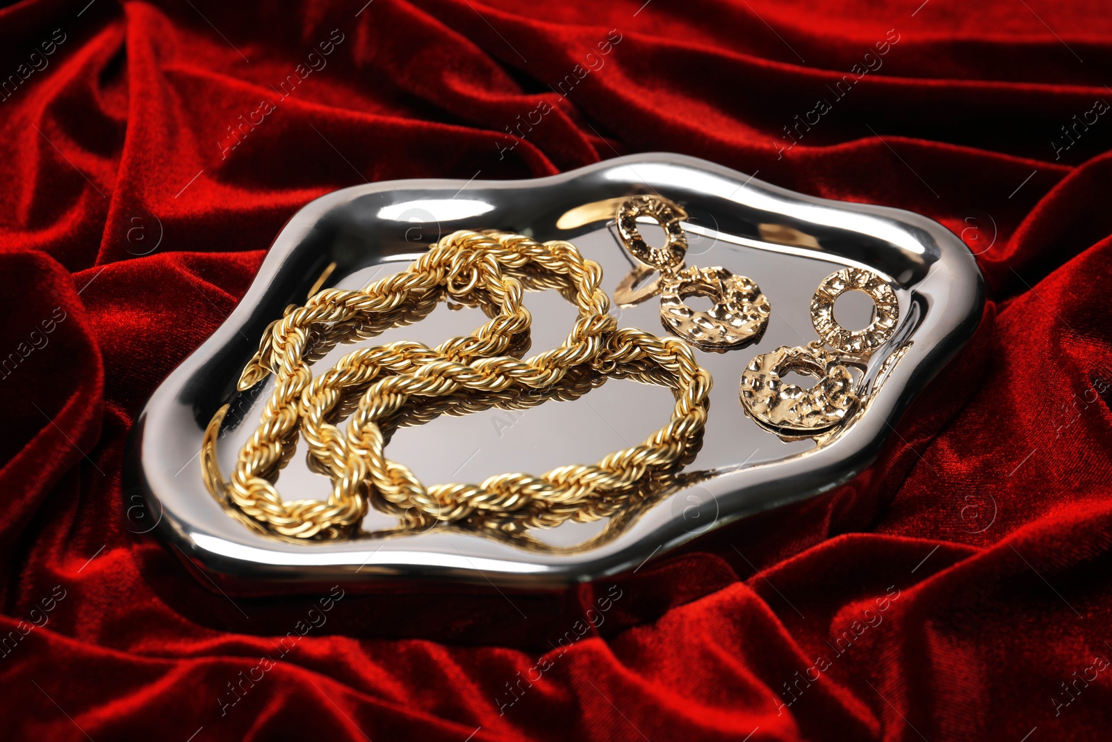 Photo of Stylish gold jewelry on red cloth, closeup