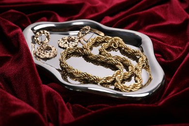 Photo of Stylish gold jewelry on red cloth, closeup