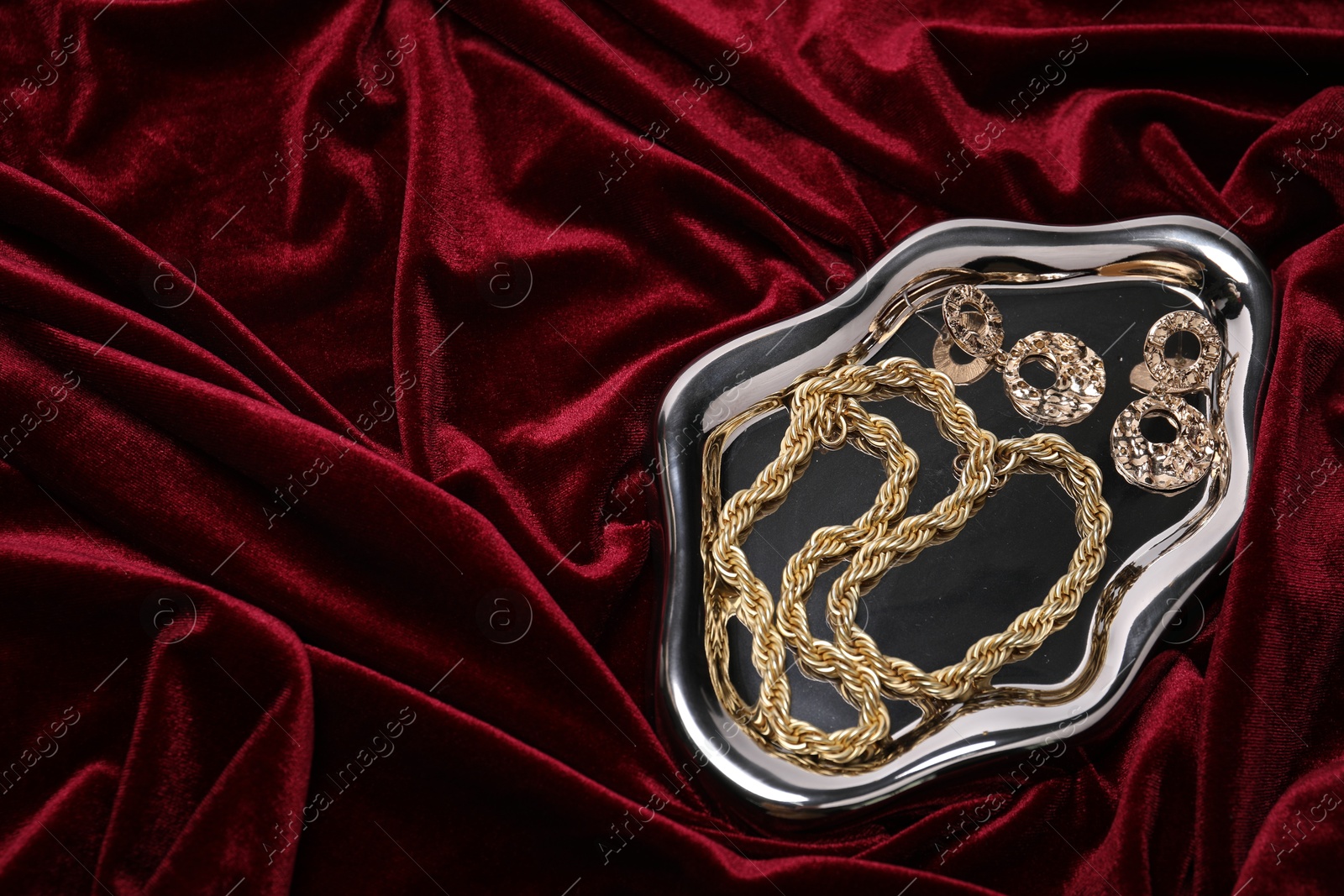 Photo of Stylish gold jewelry on red cloth, top view. Space for text