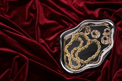 Photo of Stylish gold jewelry on red cloth, top view. Space for text