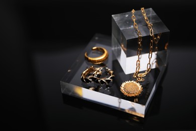 Photo of Stylish presentation of gold jewelry on black mirror surface, closeup. Space for text