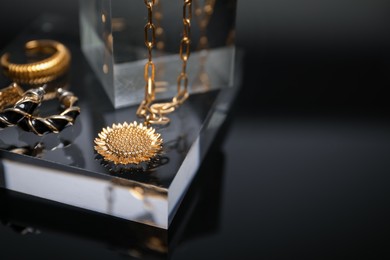 Photo of Stylish presentation of gold jewelry on black mirror surface, closeup. Space for text