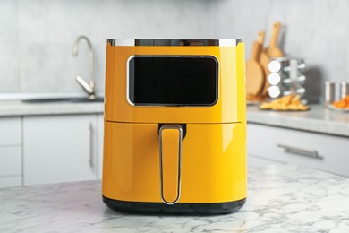 Photo of Modern yellow air fryer on white marble table in kitchen