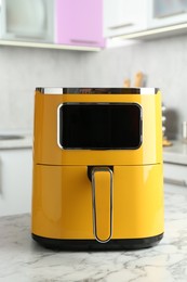 Photo of Modern yellow air fryer on white marble table in kitchen