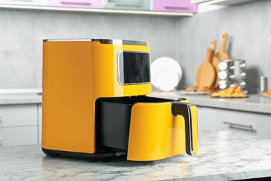 Photo of Modern yellow air fryer on white marble table in kitchen