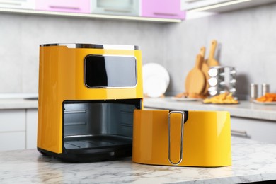 Photo of Modern yellow air fryer on white marble table in kitchen