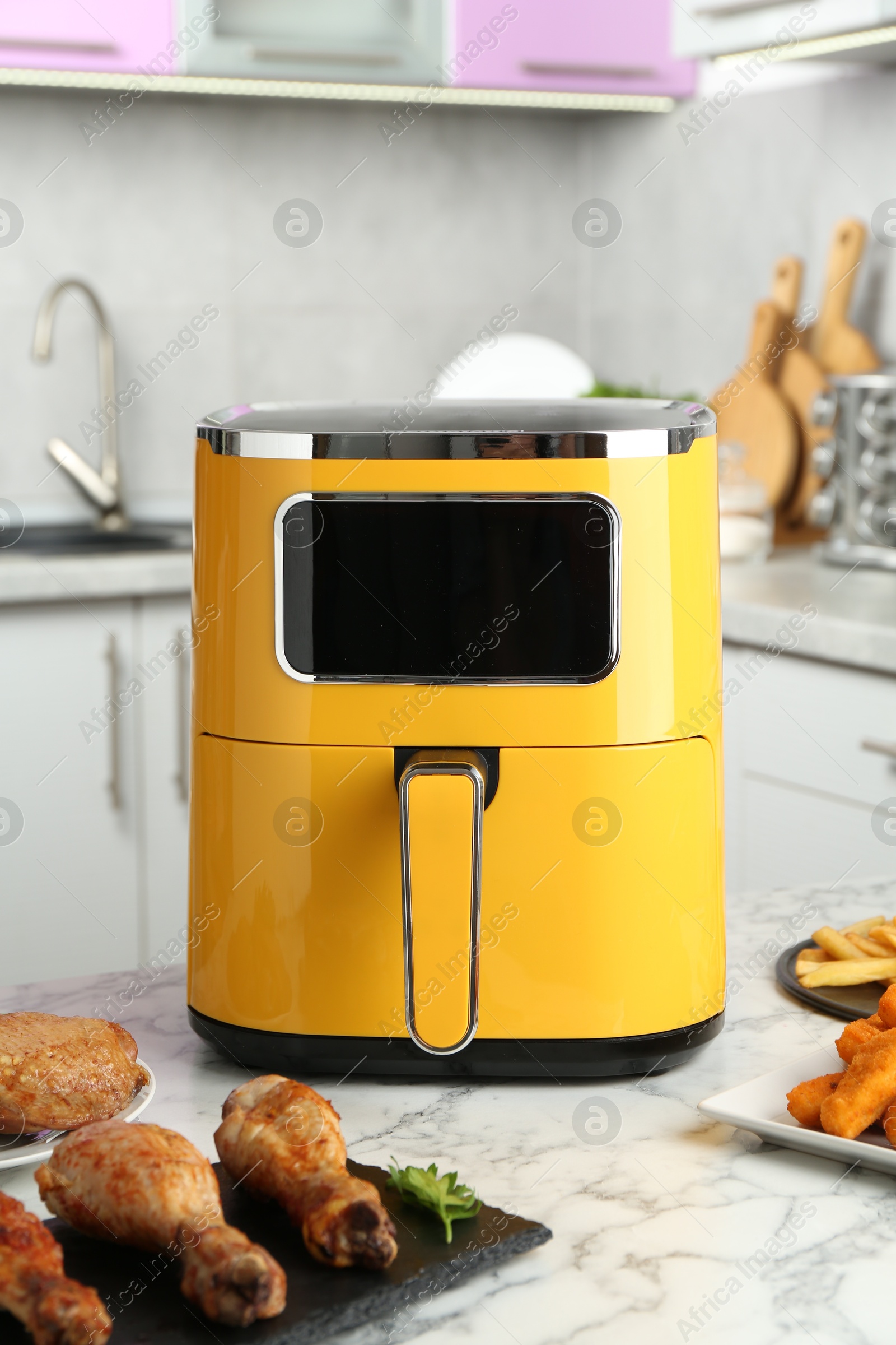 Photo of Modern air fryer and cooked meals on white marble table in kitchen
