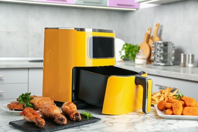 Photo of Modern air fryer and cooked meals on white marble table in kitchen