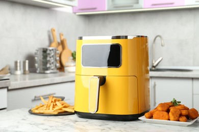 Photo of Modern air fryer and cooked meals on white marble table in kitchen