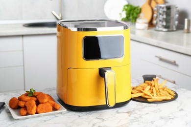 Photo of Modern air fryer and cooked meals on white marble table in kitchen