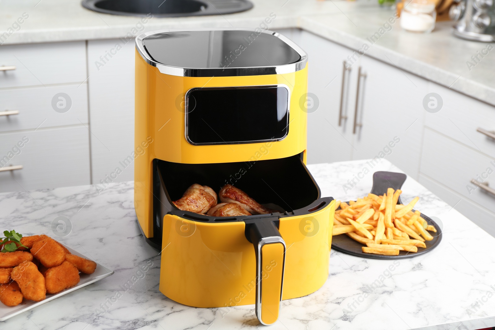 Photo of Modern air fryer and cooked meals on white marble table in kitchen
