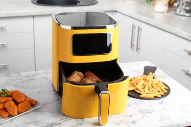 Photo of Modern air fryer and cooked meals on white marble table in kitchen
