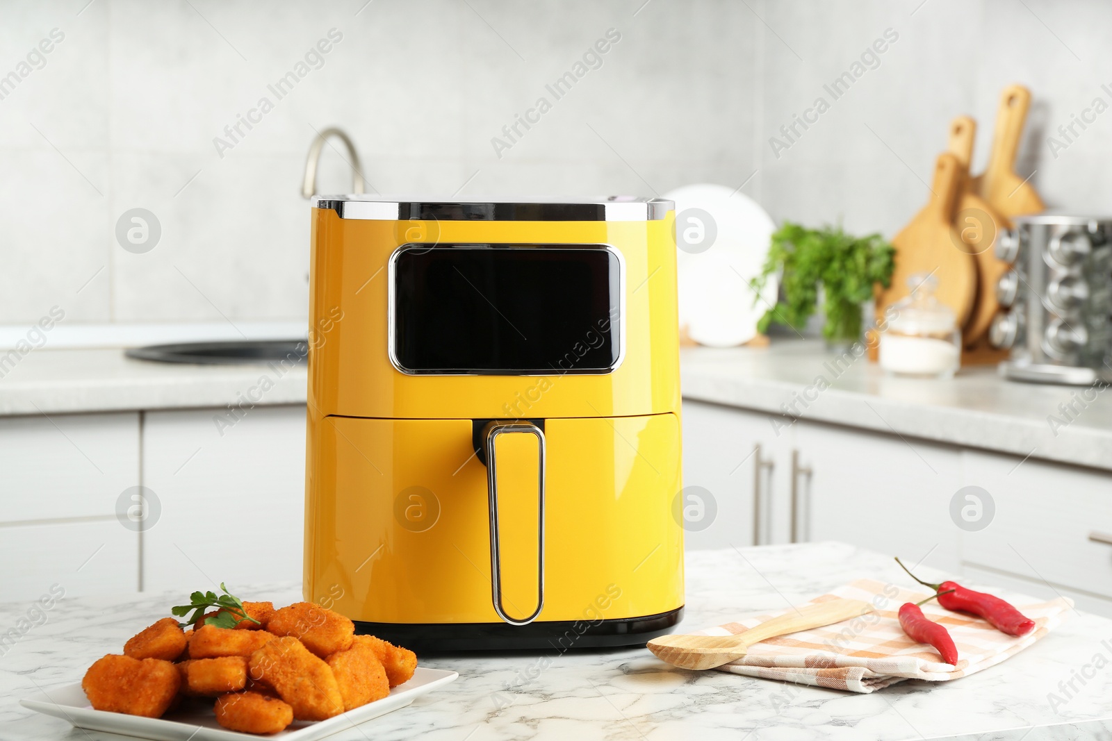 Photo of Air fryer and cooked chicken nuggets on white marble table in kitchen