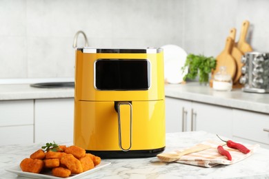 Photo of Air fryer and cooked chicken nuggets on white marble table in kitchen