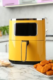 Photo of Air fryer and cooked chicken nuggets on white marble table in kitchen