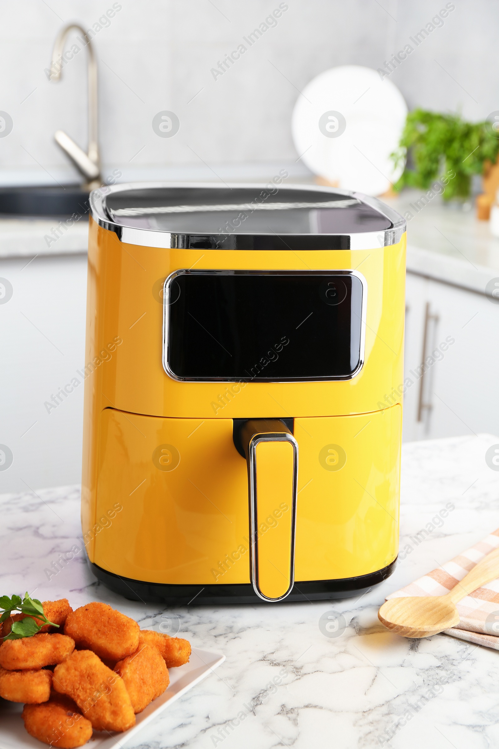 Photo of Air fryer and cooked chicken nuggets on white marble table in kitchen