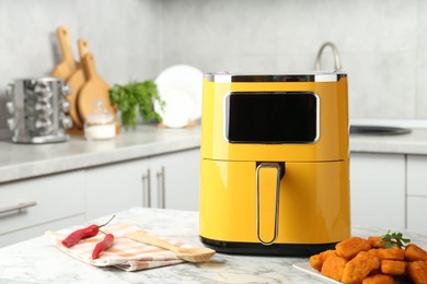 Photo of Air fryer and cooked chicken nuggets on white marble table in kitchen