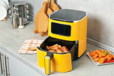 Photo of Air fryer with cooked chicken drumsticks and nuggets on counter in kitchen