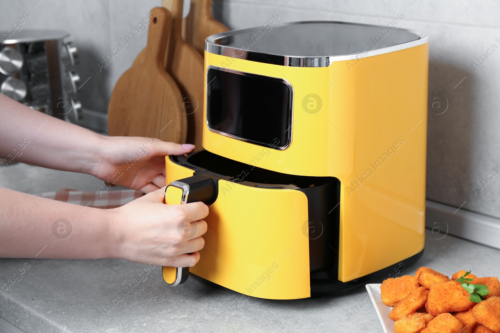 Photo of Woman taking out air fryer basket at counter in kitchen, closeup