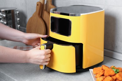 Photo of Woman taking out air fryer basket at counter in kitchen, closeup
