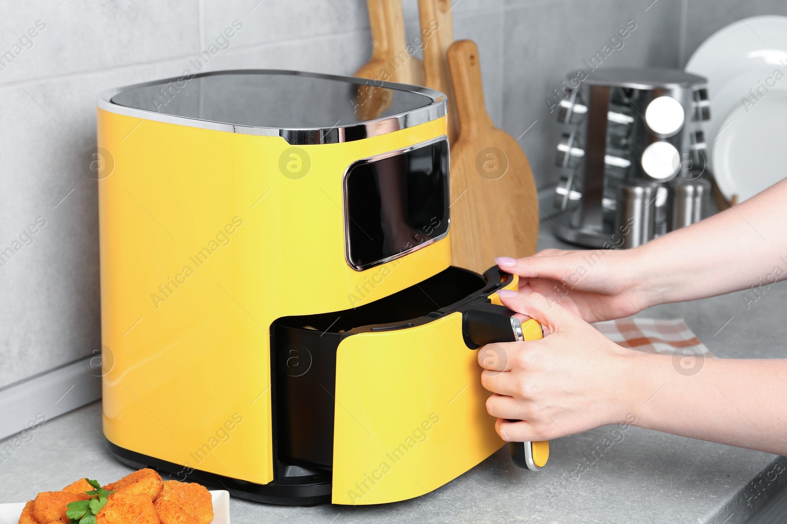 Photo of Woman taking out air fryer basket at counter in kitchen, closeup