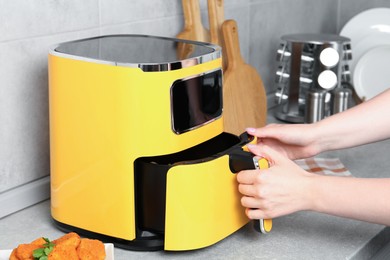 Photo of Woman taking out air fryer basket at counter in kitchen, closeup
