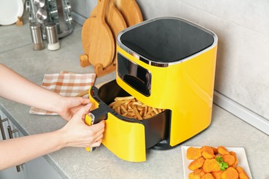 Photo of Woman taking out air fryer basket at counter in kitchen, closeup