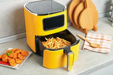 Photo of Air fryer with cooked fries and chicken nuggets on counter in kitchen
