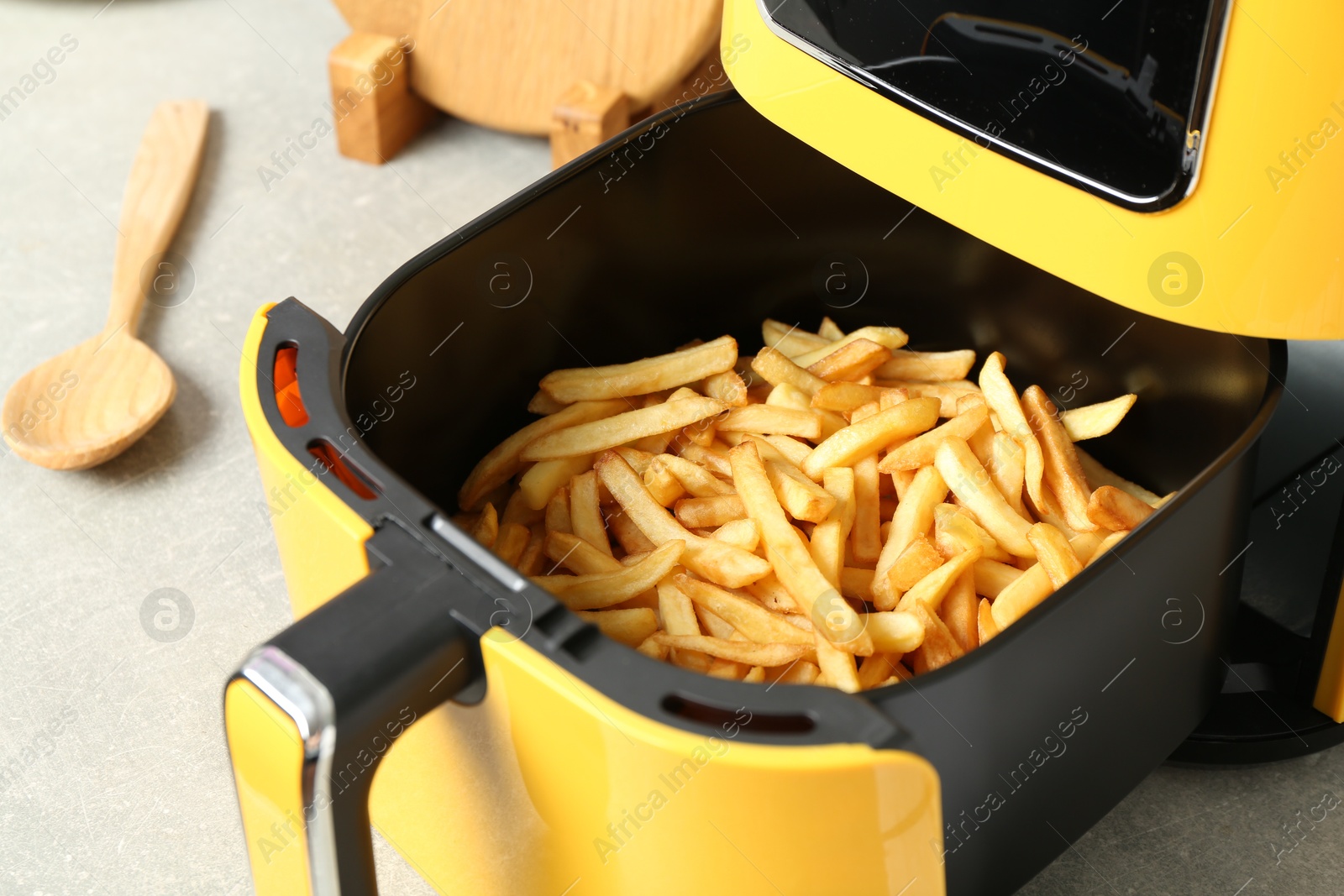 Photo of Air fryer with cooked fries on light table, closeup