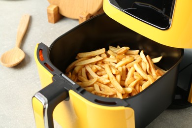 Photo of Air fryer with cooked fries on light table, closeup