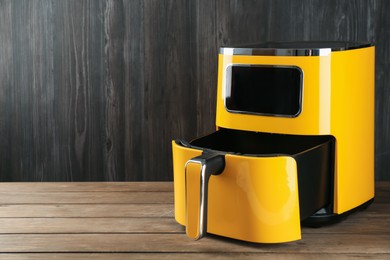 Photo of Modern yellow air fryer on wooden table. Space for text