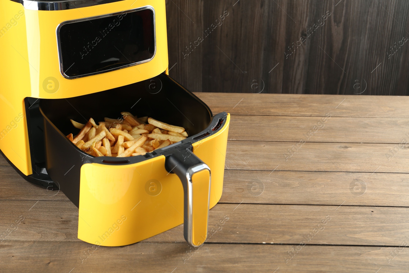 Photo of Air fryer with cooked fries on wooden table. Space for text