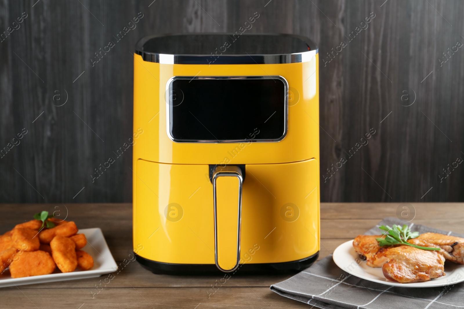Photo of Modern air fryer and cooked meals on wooden table