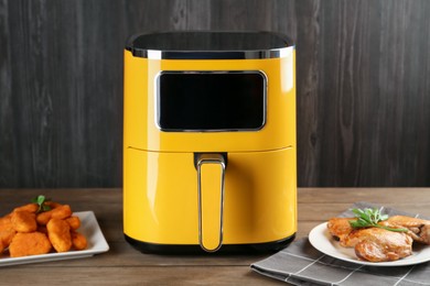 Photo of Modern air fryer and cooked meals on wooden table