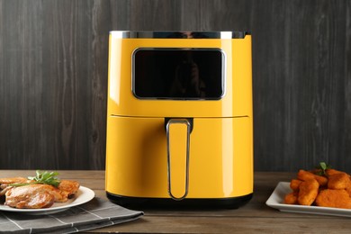 Photo of Modern air fryer and cooked meals on wooden table