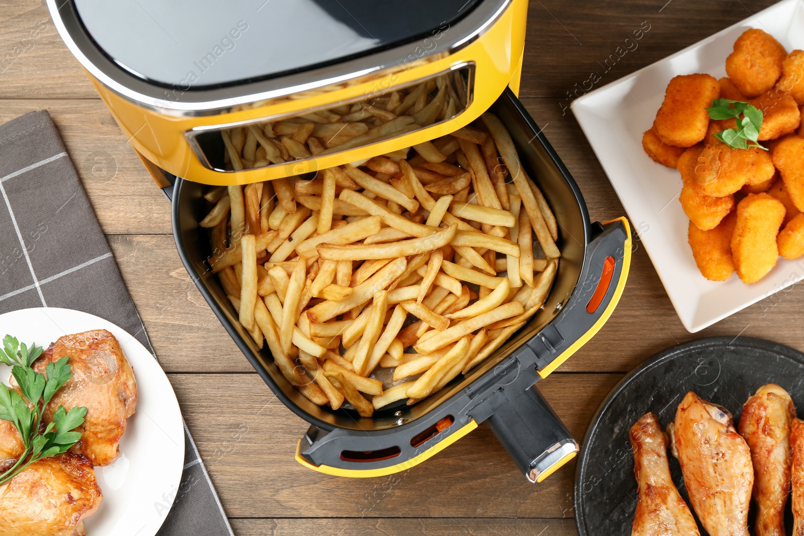 Photo of Modern air fryer and cooked meals on wooden table, flat lay