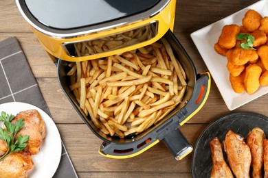 Photo of Modern air fryer and cooked meals on wooden table, flat lay