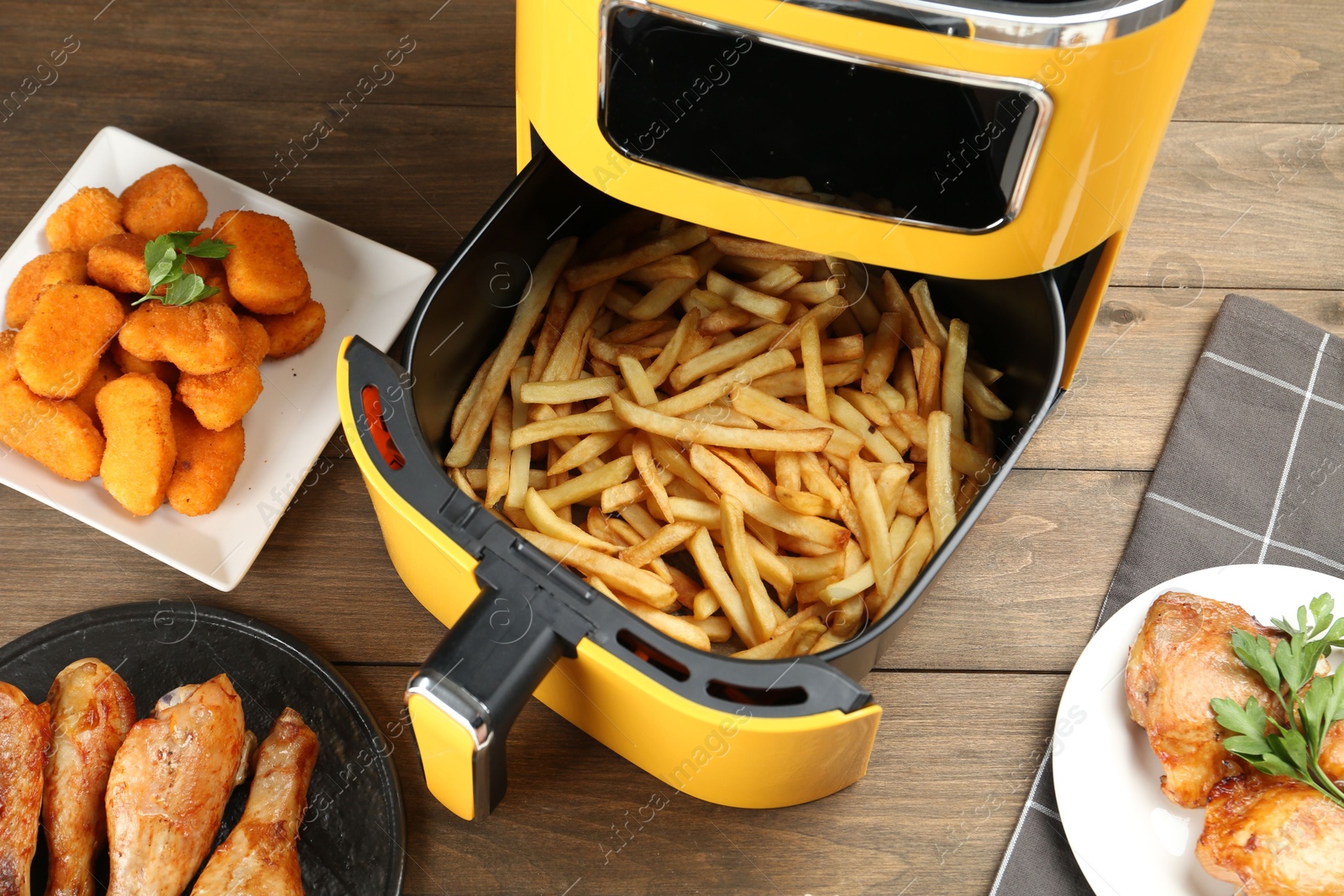 Photo of Modern air fryer and cooked meals on wooden table, flat lay