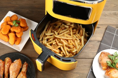 Photo of Modern air fryer and cooked meals on wooden table, flat lay