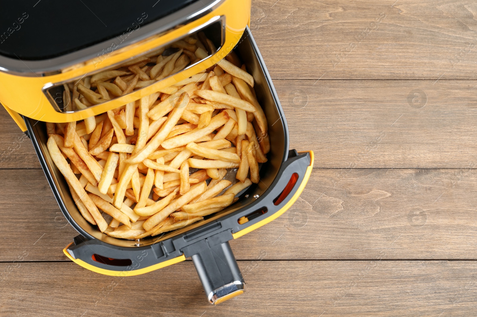 Photo of Air fryer with cooked fries on wooden table, top view. Space for text