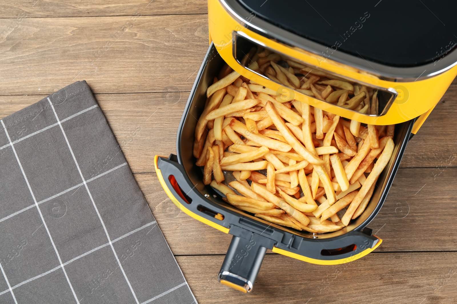 Photo of Air fryer with cooked fries on wooden table, top view