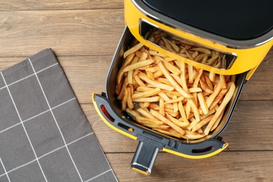Photo of Air fryer with cooked fries on wooden table, top view