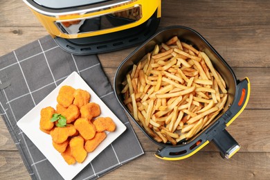 Photo of Air fryer with cooked fries and chicken nuggets on wooden table, flat lay