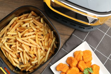 Photo of Air fryer with cooked fries and chicken nuggets on wooden table, flat lay