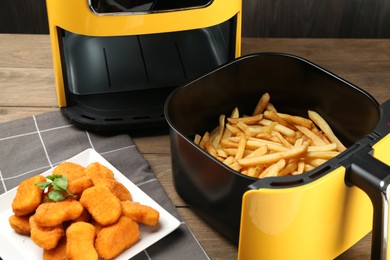Photo of Air fryer with cooked fries and chicken nuggets on wooden table, closeup