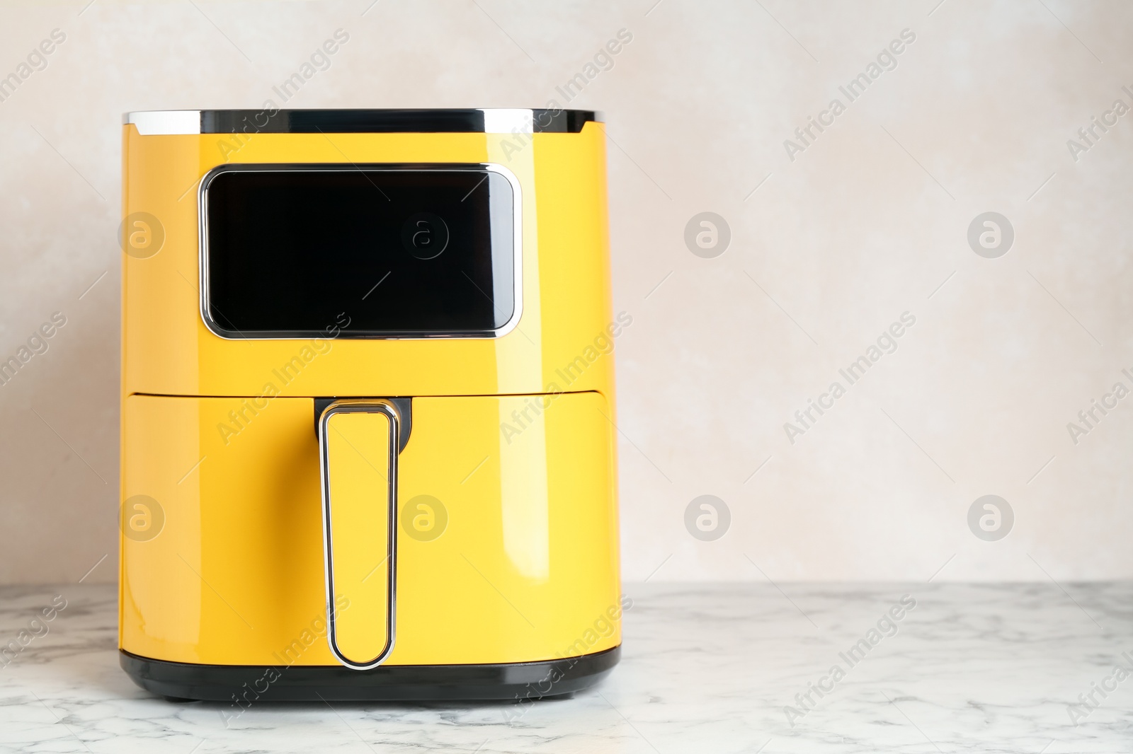 Photo of Modern yellow air fryer on white marble table. Space for text