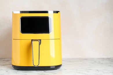 Photo of Modern yellow air fryer on white marble table. Space for text
